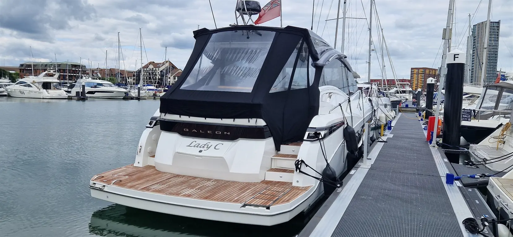 Galeon yacht named "Lady C" docked at the marina, showcasing a black canopy, polished wood deck, and nearby boats.